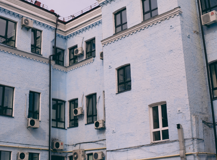 Window air conditioners dot the outside of a blue-brick apartment building