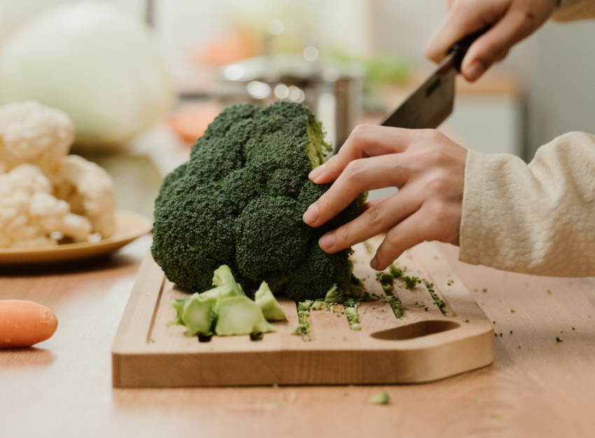 A hand slices a stalk of broccoli that's on a wooden chopping board