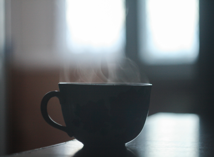 A dark tea cup sits on a table with steam rising from it.
