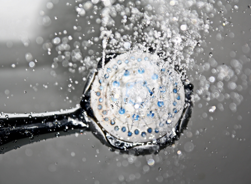 A black showerhead sprays water towards the camera. The water droplets catch the light.