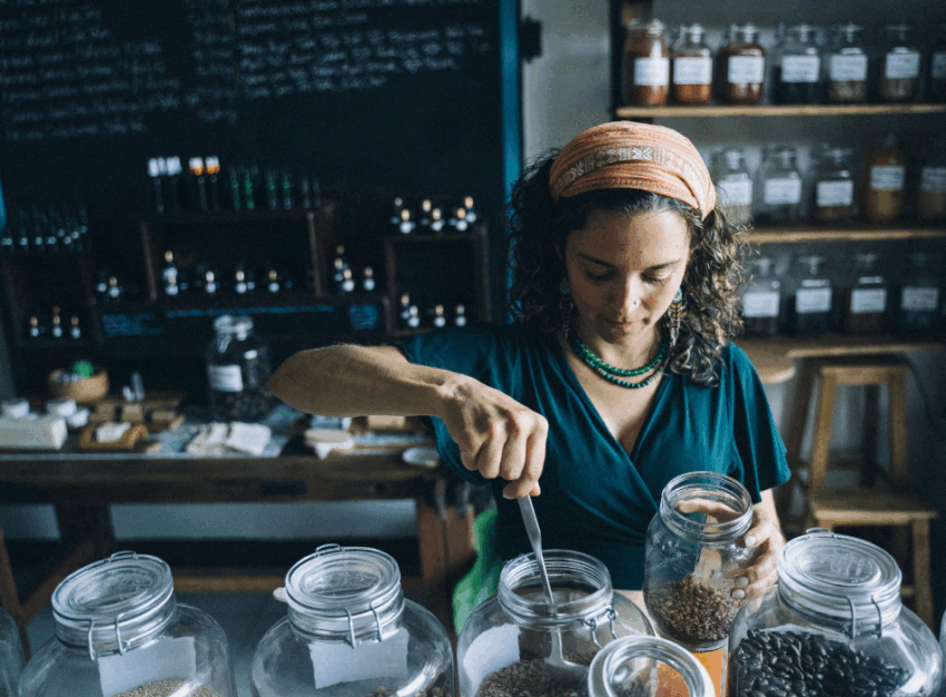 A woman scoops legumes into a jar at a bulk store.