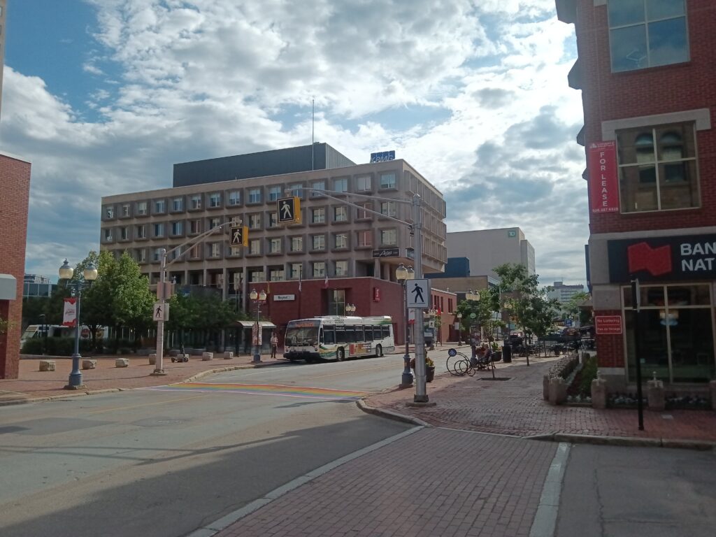An intersection in downtown Moncton with crosswalks, office buildings and a bus in the distance.