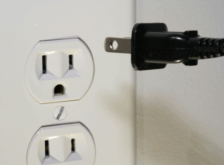 A wall outlet with the plug for an electronic device hovering nearby.