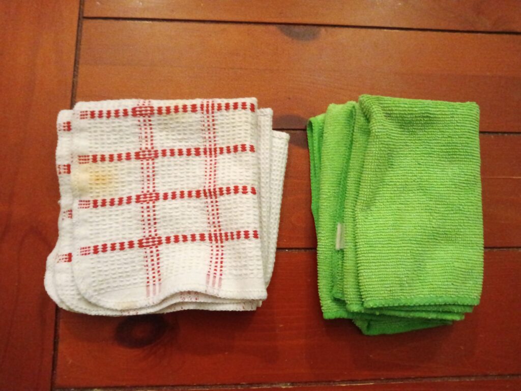 A white cloth with red stripes and a green cloth sit next to each other on a wooden surface.