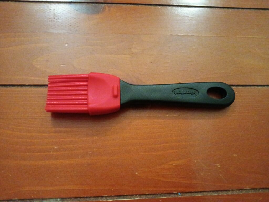 A silicone pastry brush with red bristles sits on a wooden surface.