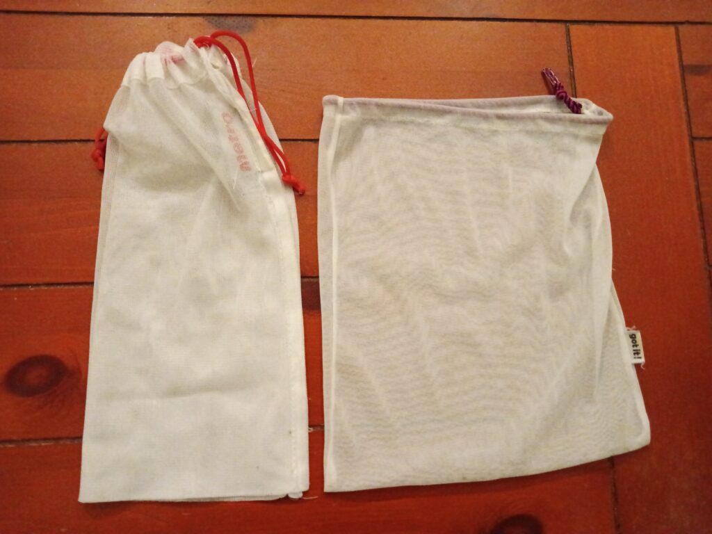 Two cotton mesh produce bags sit on a wooden surface.