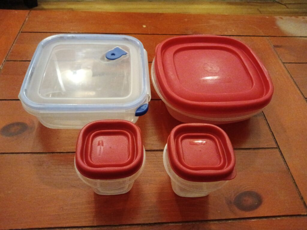 Two large reusable plastic containers and two small reusable containers sit on a wooden surface.
