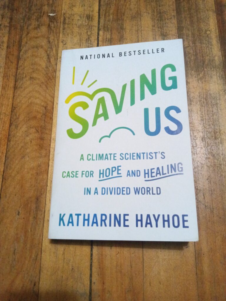 The book Saving Us by Katharine Hayhoe sitting on a wood floor.