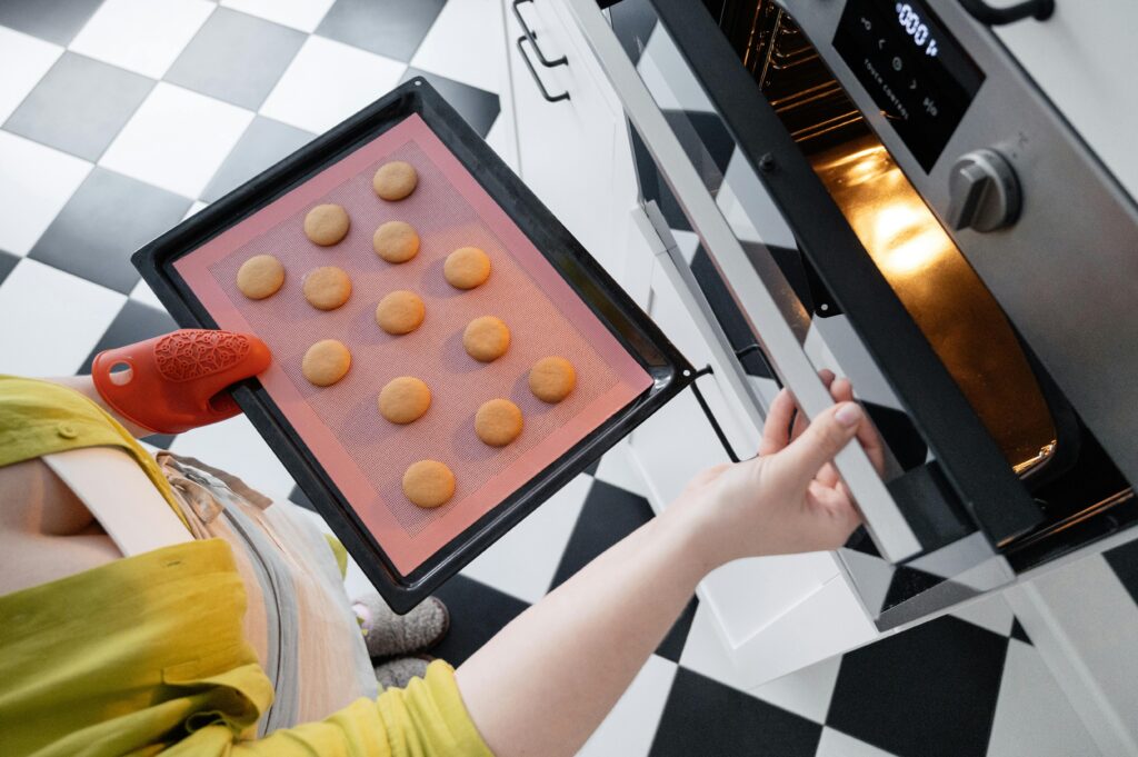 A woman sticks a baking tray containing a silicone baking mat and cookies in an oven.