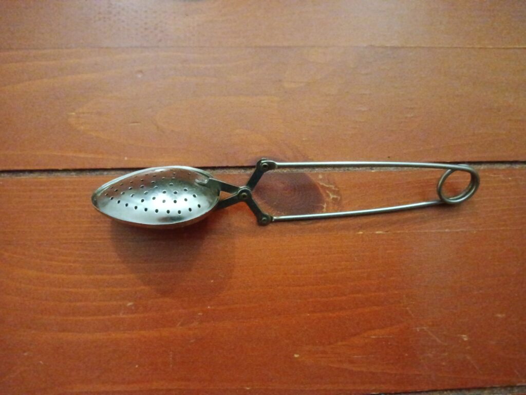 A metal tea strainer that clips closed sits on a wooden surface.