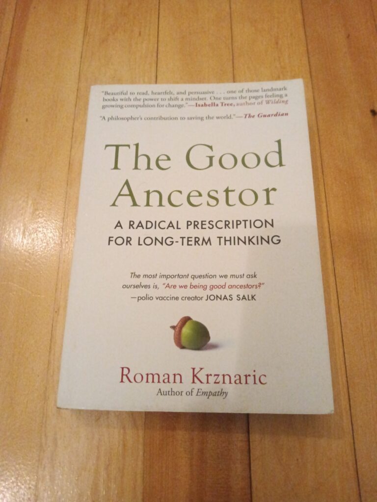 The book The Good Ancestor by Roman Krznaric sitting on a wood floor.