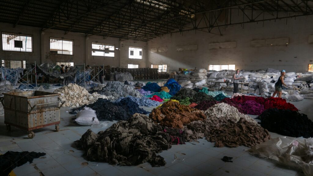 Piles of clothing waste sit on the floor of a warehouse.