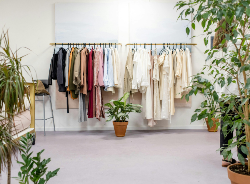 A clothing rack containing clothes of various colours, framed by potted plants.