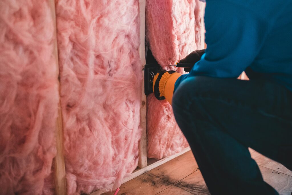 A worker adjusts the pink insulation in a wall.