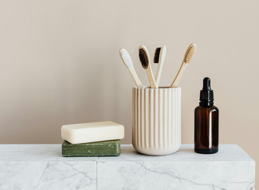 Two bars of soap, a cup containing bamboo toothbrushes and a dark-brown dropper bottle sit on a marble surface.