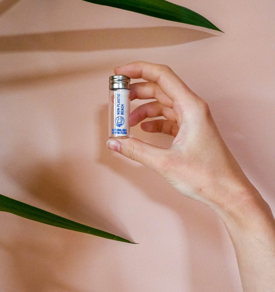 A person holds a small glass vial containing silk dental floss.