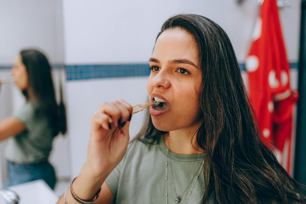 A woman with long dark hair brushes her teeth using a bamboo toothbrush.