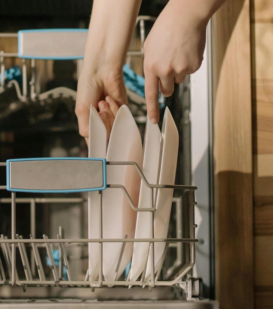 A person loads two plates into a dishwasher.