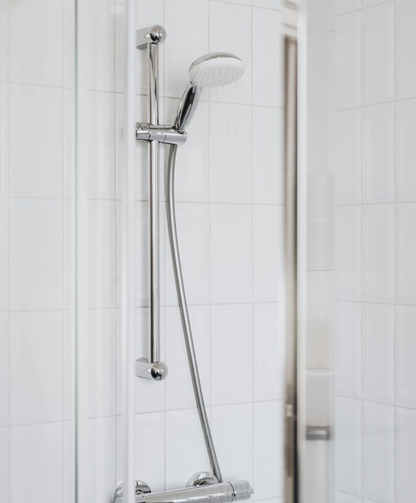 Water comes out of the showerhead in a shower with white tile walls.