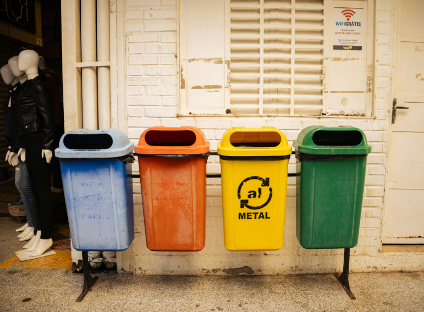 Four vertical recycling bins in a row of different colours (blue, red-orange, yellow and green).