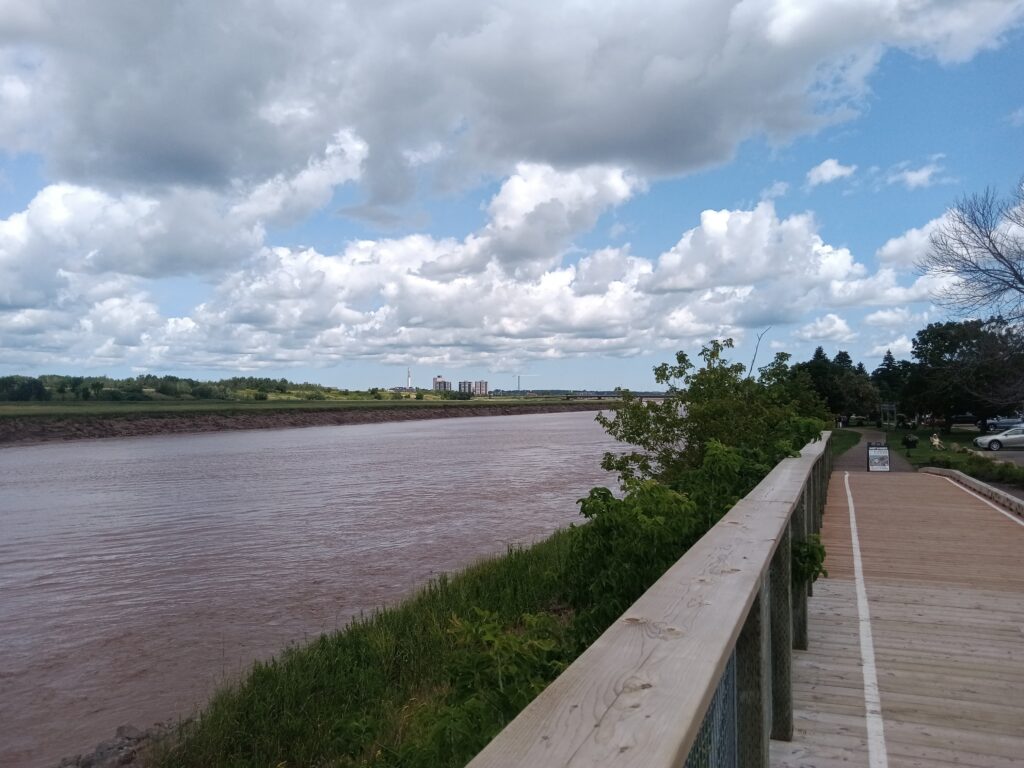 A boardwalk next to a muddy river. The sky is blue with a few clouds.